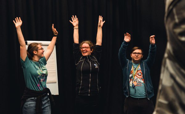 Three young people raise their arms in the air, smiling and laughing at each other