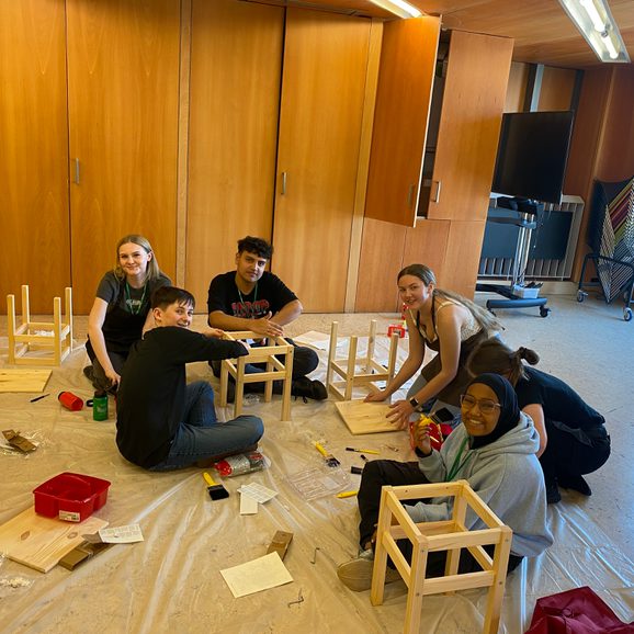 A diverse group of young people paint stools that are part of a stage set during Cast's Work Experience Week.
