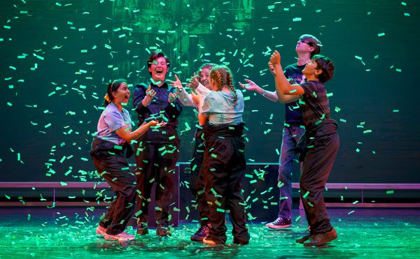 Six young performers on stage are light by a emerald green light as confetti falls to the ground and the jump in exhilaration. This photo is from the 2023 Cast Youth Theatre production of Time Casters.