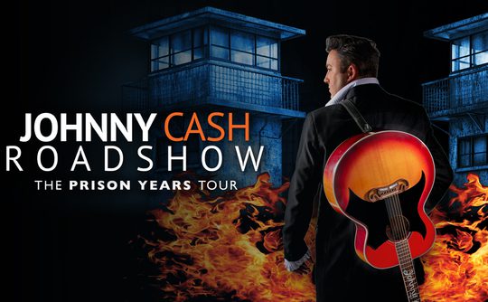 "Johnny Cash Roadshow poster features a man in a suit with a guitar on his back, standing before a prison backdrop with flames, evoking intensity."