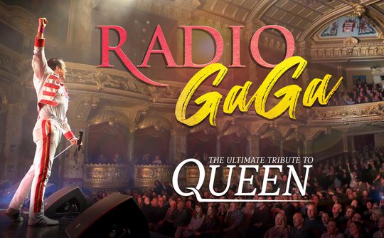 Performer in a white and red outfit raises a fist on stage. Background features an ornate theatre with an audience. Text reads "Radio GaGa: The Ultimate Tribute to Queen."