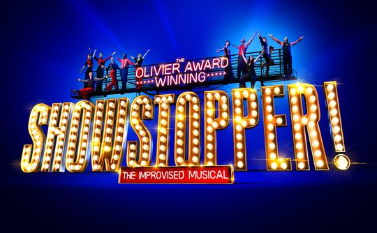 Olivier Award-winning "Showstopper! The Improvised Musical" logo features people dancing above large illuminated letters on a vibrant blue background.