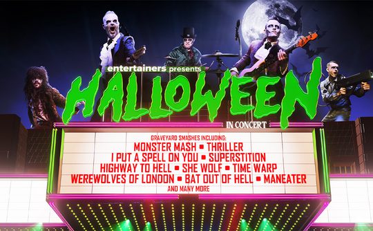 A cinema at night with a sign that reads "Entertainers Presents Halloween In Concert" with a glowing green font. A full moon shines brightly above and spookily dressed performers are superimposed behind the title. Dramatic Halloween vibes.