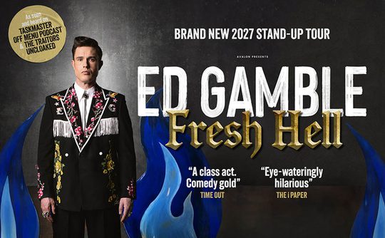 Comedian in a floral embroidered suit stands before a backdrop of stylized blue flames. Text reads "Ed Gamble: Fresh Hell" for the 2027 stand-up tour.