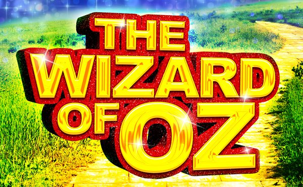Bold, glittering red-and-gold “The Wizard of Oz” title fills the scene above a yellow brick road through vivid green fields under a sparkling blue sky.