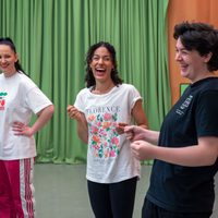 Three people stand in front of a green curtain, smiling and laughing. They're wearing casual clothes, exuding a joyful and relaxed atmosphere.