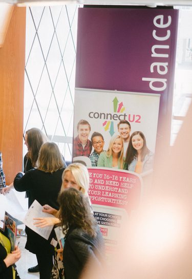 Students and teachers stand around different banners advertising apprenticeship opportunities.