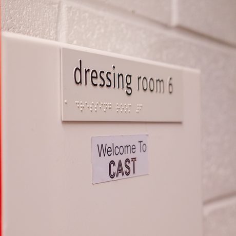 Red door jam appears in the foreground next to a sign that reads "dressing room 6" and another sticker underneath that reads "Welcome to Cast"