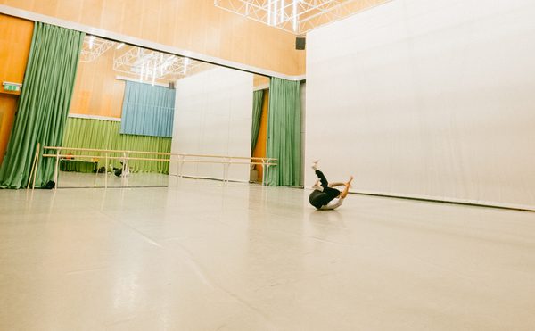 The spacious Dance Space at Cast with high ceilings and bright lights. A dancer lies on the floor mid-move, surrounded by mirrors and green curtains. The mood is focused and artistic.