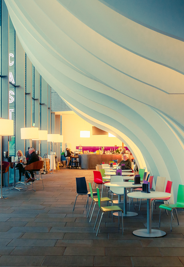 Cast building interior at dusk, low level lighting and round tables and coloured chairs featured