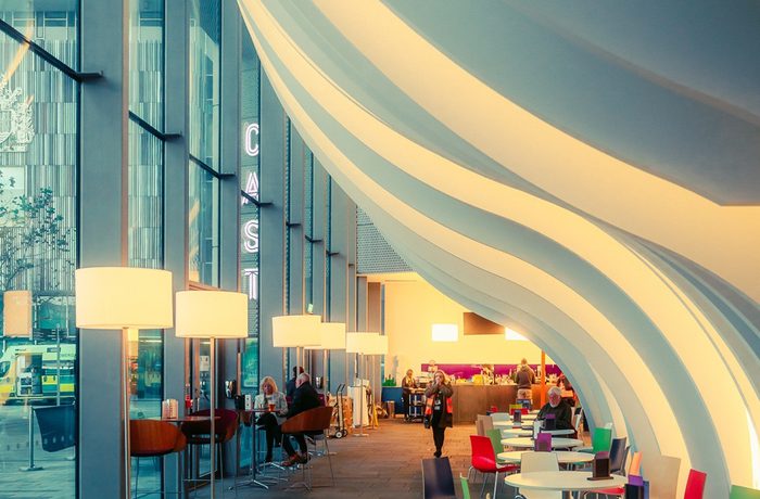 Cast building interior at dusk, low level lighting and round tables and coloured chairs featured
