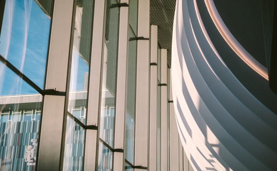 An artistic shot of the Cast foyer from a low angle, the curve of the building and the full height windows are the main feature, with the sky and council building in the distance