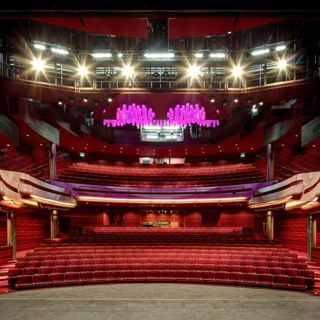 The modern auditorium in Cast's Main Space with red seating and luxurious wood paneling. A striking purple chandelier hangs from the ceiling, creating an elegant atmosphere.