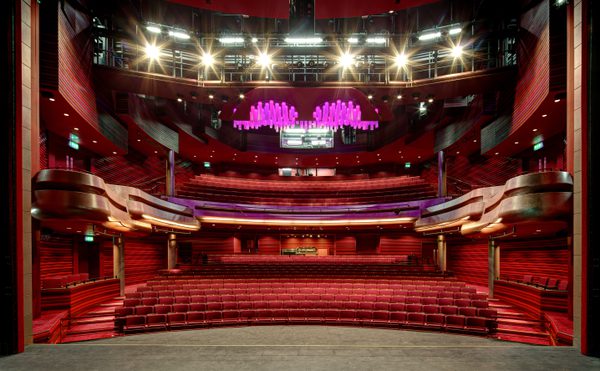 The modern auditorium in Cast's Main Space with red seating and luxurious wood paneling. A striking purple chandelier hangs from the ceiling, creating an elegant atmosphere.