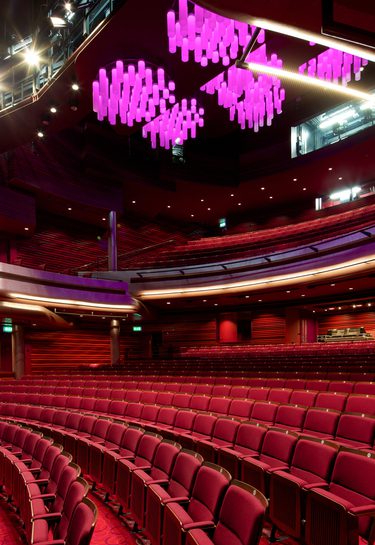 Interior of Cast's modern Main Space auditorium with curved rows of red seats, a spacious stage, and unique purple chandeliers, creating an elegant atmosphere.