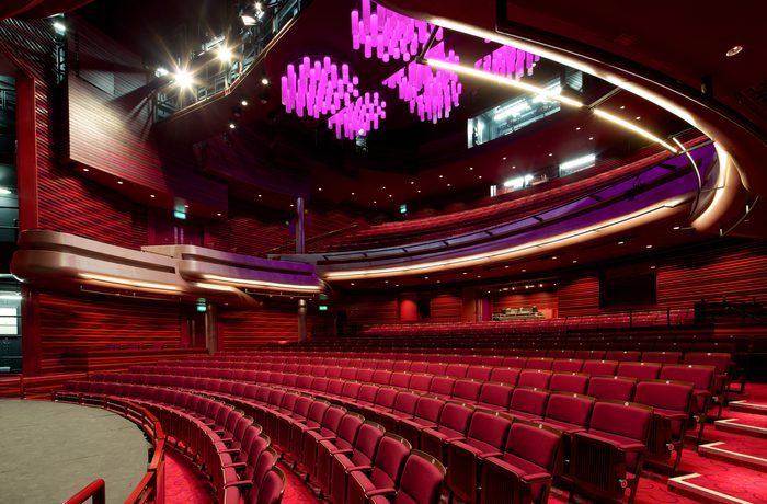 Interior of Cast's modern Main Space auditorium with curved rows of red seats, a spacious stage, and unique purple chandeliers, creating an elegant atmosphere.