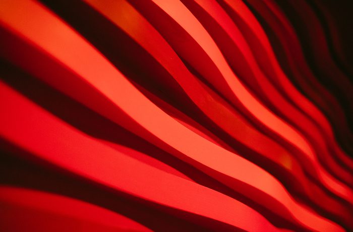 Abstract image of wavy red lines creating a dynamic, flowing pattern along the walls of Cast's Main Space auditorium. The lighting casts dramatic shadows, giving a sense of movement and energy.