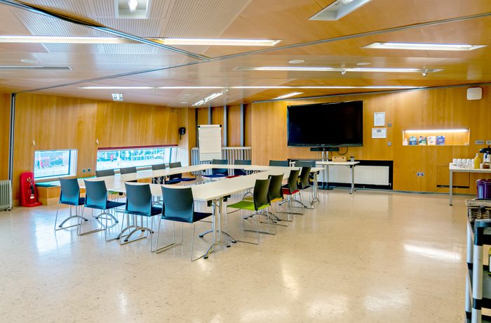 Cast's modern conference room Meeting Space with a rectangular-shaped arrangement of white tables and colorful chairs, a large TV screen, flip chart stand, and refreshment table.